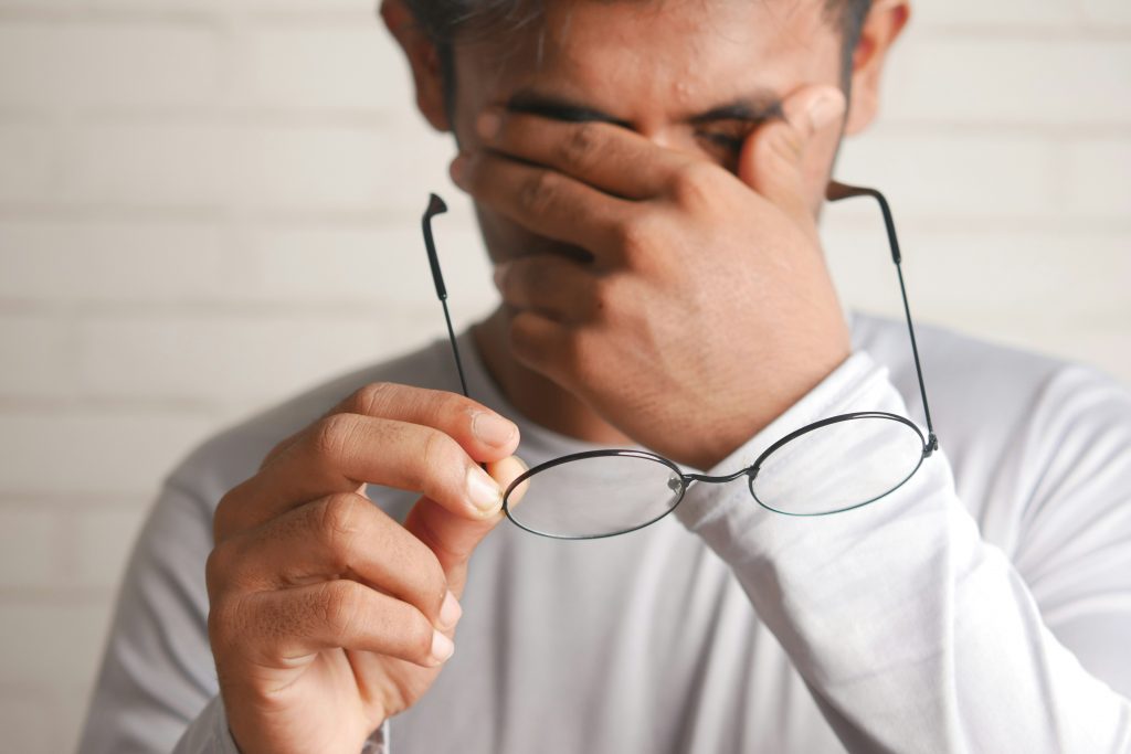 Erschöpfter Arbeitnehmer hält seine Brille und reibt sich die Augen – Symbolbild zum Thema krank mit Ankündigung und Verdachtskündigung bei Kanzlei Könemann.