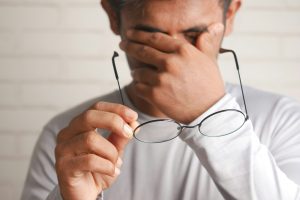 Erschöpfter Arbeitnehmer hält seine Brille und reibt sich die Augen – Symbolbild zum Thema krank mit Ankündigung und Verdachtskündigung bei Kanzlei Könemann.